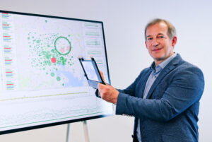 Raimund Dachselt standing infront of a large screen while holding the CleAR Sight research prototype