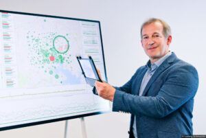 Raimund Dachselt standing infront of a large screen while holding the CleAR Sight research prototype
